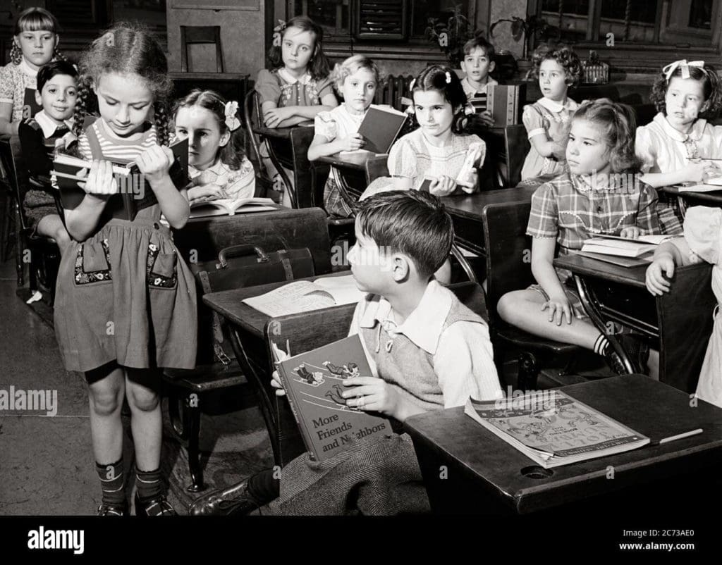 1950s elementary school classroom girl student standing by desk reading aloud from textbook to rest of the class s8066 har001 hars grade textbook knowledge leadership pride primary connection conceptual